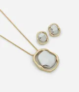 Conjunto de collar largo con cadena dorada y colgante abstracto con baño mixto dorado y plateado, y aros de botón con la misma forma que el colgante.