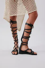 Sandalia de tipo gladiador en color negro, con tiras entrelazadas y tacón bajo.