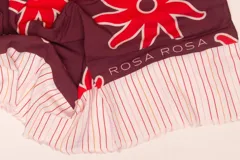 Pareo rectangular de viscosa con estampado de flores rojas sobre fondo borgoña y borde inferior con rayas verticales rojas, amarillas y blancas.