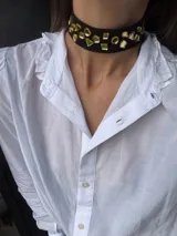 Gargantilla negra con base de tela y apliques de acrílico dorado con formas geométricas.