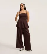 Pantalón de mujer color marrón oscuro, de tiro alto con cintura elástica fruncida y corte ancho recto. Presenta vincos delanteros marcados.