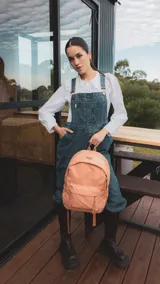 Mochila de tela color salmón con bolsillo frontal con cierre, bolsillos laterales con elástico y bolsillo trasero con cierre. Tiene correas acolchadas y cómodas.