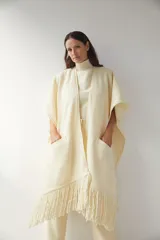 Ruana color crema de lana fina con flecos en el ruedo y bolsillos delanteros.