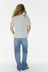 Camiseta gris de algodón con cuello redondo y manga corta. Tiene apliques de strass plateado en el frente.