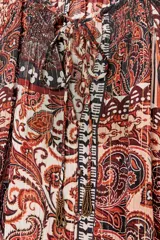 Blusa marrón con estampado de cachemir y detalles de hilo metalizado. Tiene cuello redondo con cordón ajustable y abalorios, escote en pico con nido de abeja, mangas largas con elástico en los puños y cierre frontal con botones forrados.