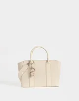 Cartera tipo tote color blanco crudo, con doble asa corta y correa larga regulable y desmontable. Incluye charm colgante con forma de corazón y cierre superior.