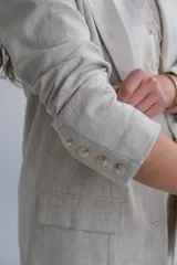 Blazer beige de lino, con solapas de muesca, cierre frontal con dos botones y bolsillos laterales con solapa.