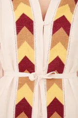 Saco color crema con bordado de flechas en tonos amarillo, marrón y rojo. Tiene mangas largas con detalle de puntilla y cinturón fino del mismo tejido.