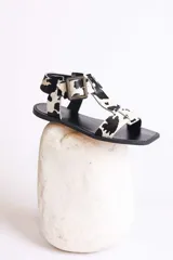 Sandalias planas con tiras de cuero con estampado de vaca en blanco y negro, y hebilla lateral.