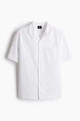 Camisa blanca de manga corta en mezcla de algodón y lino. Modelo con cuello abierto, tapeta lisa y bolsillo superior abierto.