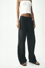 Pantalón negro de tiro alto con cintura elástica, bolsillos delanteros y detalle de banda lateral blanca.