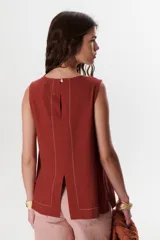 Top sin mangas color terracota con cuello redondo y bolsillo frontal. Presenta costuras a contratono en blanco que definen los bordes y el bolsillo.