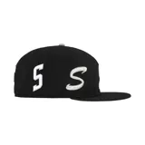 Gorra negra de la colaboración Supreme x New Era, modelo 59Fifty, con logo "S" en blanco en el frente, logo de Supreme bordado en el lateral y logo de New Era en el otro lateral.