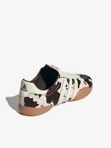 Zapatillas Adidas Taekwondo Mei sin cordones, con capellada de cuero vacuno con estampado animal print de vaca, las tres tiras características de la marca en cuero blanco y suela de goma color caramelo.