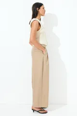 Pantalón color beige de corte holgado con silueta baggy. Modelo de tiro alto con pinzas, elástico revestido en la cintura, cierre y pretina prolongada con botón y corchete ocultos. Bolsillos al bies y bolsillos decorativos atrás.