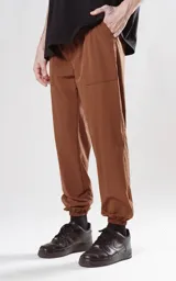 Pantalón multifuncional impermeable color marrón, con elástico en la cintura y puños, y bolsillos frontales.