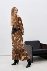 Vestido largo de viscosa estampada en tonos marrón y beige, con escote en V, mangas largas con puños elásticos y volado en el ruedo. Incluye lazo del mismo género para ajustar en la cintura.