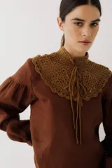 Blusa color ladrillo con cuello alto de crochet y lazos para ajustar. Mangas largas abullonadas con puños elásticos.