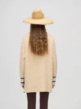 Sweater color crema con tejido en ochos, cuello redondo, puños acanalados con doble raya azul y tajos a los costados.