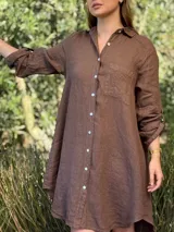 Vestido camisero blanco de lino, con cuello camisero, manga larga con botón para recoger, cierre frontal con botones de nácar, bolsillo en el pecho y diseño asimétrico más largo en la parte trasera.