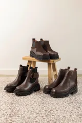 Botines negros de cuero con caña baja, puntera redondeada y cierre frontal con cremallera. Presentan paneles laterales de gamuza y suela track con plataforma.