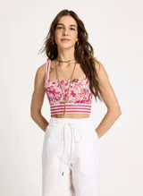 Crop top con estampado floral en tonos fucsia y blanco, breteles finos con lazos en los hombros y detalle de franjas horizontales en el bajo.