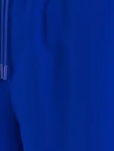 Bañador azul eléctrico de largo medio, con cintura elástica ajustable con cordón, ribete naranja en la cintura y logo de Tommy Hilfiger bordado en la parte trasera.