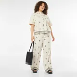 Pantalón ancho color beige con bordado de cruces negras.