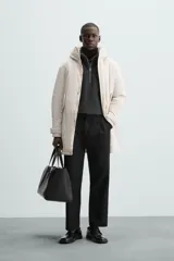 Parka color crudo de tejido técnico acolchado, con cuello alto y capucha ajustable. Tiene mangas largas con puños ajustables, bolsillos frontales con solapa, bolsillo interior y cierre frontal con cremallera oculta por solapa con botones a presión.