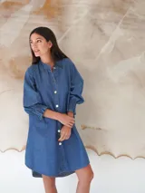 Vestido camisero corto de denim celeste, con cuello mao, mangas 3/4 con elástico en los puños y cierre frontal con botones de nácar.