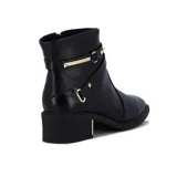 Bota de cuero negra de caña baja, con taco cuadrado y punta fina. Presenta dos tiras con hebillas doradas y apliques de tachas piramidales alrededor del tobillo. Cuenta con cierre lateral.