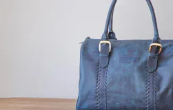 Bolso de mano azul con detalles de costuras verticales y herrajes dorados.