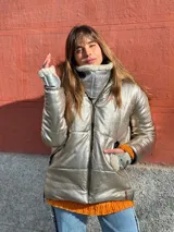Campera puffer plateada con cuello alto de piel sintética blanca, cierre frontal con cremallera y bolsillos laterales.