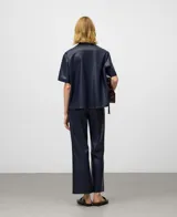 Pantalón flare de tiro alto, color azul marino oscuro, con acabado de efecto cuero. Presenta un corte ancho que se ensancha desde la rodilla hasta el tobillo.