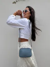 Bandolera pequeña de símil cuero color gris con textura granulada. Posee dos compartimientos principales con cierre y un bolsillo frontal con cremallera metálica. Incluye correa fina ajustable y extraíble.