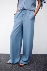 Pantalón celeste de tiro alto con cintura elástica ajustable con cordones, bolsillos delanteros y traseros, y pernera ancha.