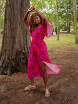 Vestido midi con estampado abstracto en tonos verde y fucsia, corte cruzado, mangas cortas amplias y lazo en la cintura.