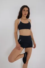 Top deportivo negro con tirantes blancos regulables, escote medio y compresión media.