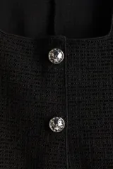 Chaleco negro de punto con textura, escote cuadrado y cierre frontal con botones metalizados con acabado martillado.