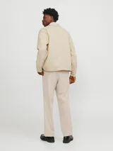 Chaqueta color crema, de manga larga, con cuello camisero y cierre frontal con cremallera metálica. Tiene dos bolsillos de parche con solapa en el pecho.