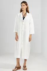 Camisa larga blanca de lino 100% italiano, con cuello clásico, mangas 3/4, silueta fluida, dobladillo curvado en las costuras laterales y bolsillos discretos.