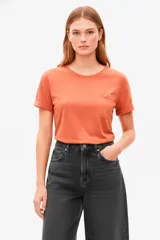 Remera de algodón color naranja quemado, manga corta con puños doblados, cuello redondo y un pequeño bolsillo en el pecho con un botón metálico.