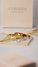 Brazalete rígido dorado con circonitas rectangulares rojas engarzadas.