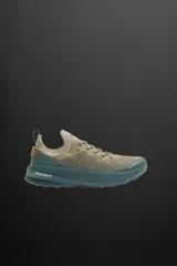 Zapatilla deportiva color arena con detalles en verde y suela azul. Fabricada en tejido de punto transpirable con puntera y talón recubiertos de material Shield Protect Max. Cuenta con ajuste mediante cordones, tirador trasero, plantilla OrthoLite® extraíble, entresuela Spume Foam V2 y suela de goma.