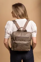 Mochila mediana de símil cuero color beige, con asa superior, dos compartimentos principales con cierre y dos bolsillos frontales con cierre. Las correas son ajustables y de color beige.