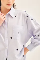 Camisa blanca de algodón con bordado de corazones dorados, corte amplio, cuello clásico, cartera con botones ocultos y bolsillo en el pecho.