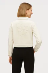 Campera corta color crudo, de corte recto, con cuello camisero, cierre frontal con botones marrones, bolsillos de parche en el pecho y mangas largas. Confeccionada en algodón.
