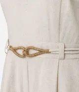 Enterito corto de mujer color beige claro, con escote en V, mangas cortas tipo capa, trabillas en la cintura y pliegues frontales. Incluye un cinturón fino trenzado de cuerda.