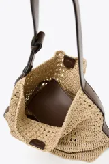 Bolso formato saca color beige, con efecto rafia en el cuerpo y asa de hombro ajustable color marrón. Incluye cartera con bolsillo extraíble y cierre mediante botón imantado.