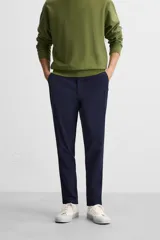 Pantalón negro de corte slim fit, confeccionado en tejido elástico. Cuenta con cintura elástica, bolsillos frontales y traseros de vivo. Cierre frontal con cremallera y botón.